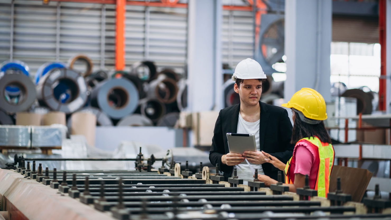 Industrial worker inspecting machine at factory machines. Technician working in the metal sheet company. Foreman checking Material or Machine. Manager consultant les données de production sur tablette avec une opératrice dans une usine métallurgique